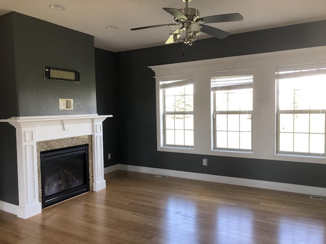 unfurnished living room with ceiling fan, a healthy amount of sunlight, a glass covered fireplace, visible vents, and wood finished floors