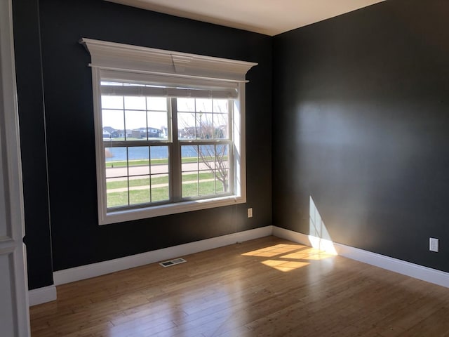spare room featuring baseboards, visible vents, and wood finished floors