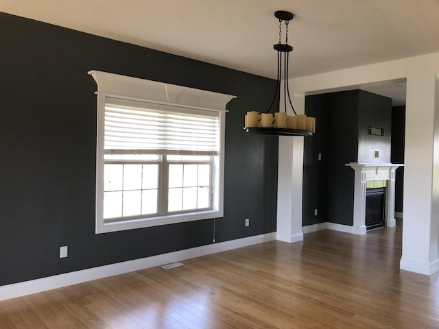 unfurnished dining area with baseboards, visible vents, wood finished floors, and a fireplace