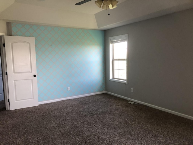 unfurnished room featuring a ceiling fan, a tray ceiling, dark colored carpet, and baseboards