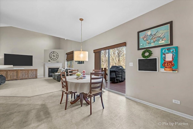 dining area featuring lofted ceiling, a glass covered fireplace, and baseboards