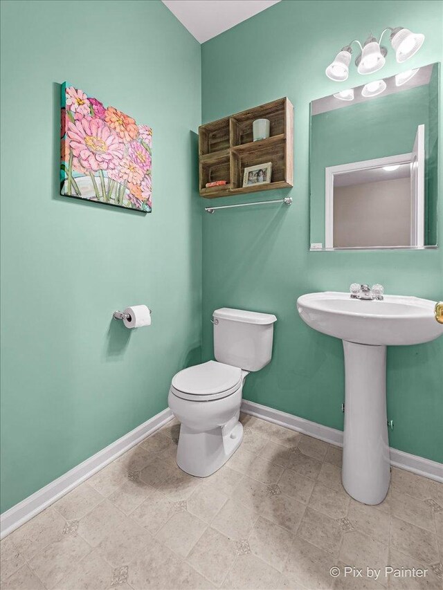 half bath with baseboards, toilet, and a sink