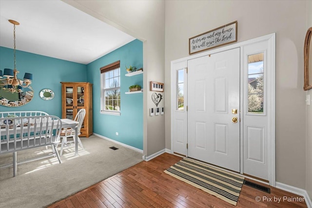 foyer entrance with visible vents, hardwood / wood-style flooring, a notable chandelier, and baseboards