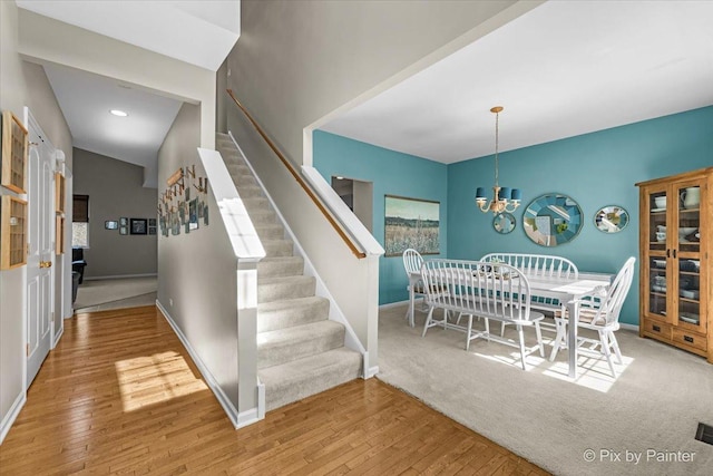 stairs featuring baseboards, an inviting chandelier, and wood-type flooring