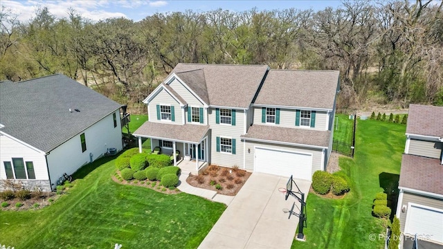 traditional home with covered porch, roof with shingles, a front yard, concrete driveway, and an attached garage