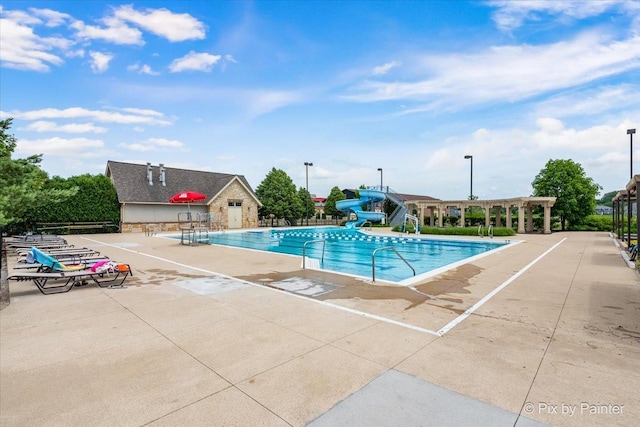community pool with a patio area, a water slide, and a pergola