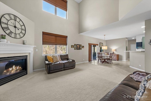carpeted living area with a towering ceiling, recessed lighting, a fireplace with flush hearth, and baseboards