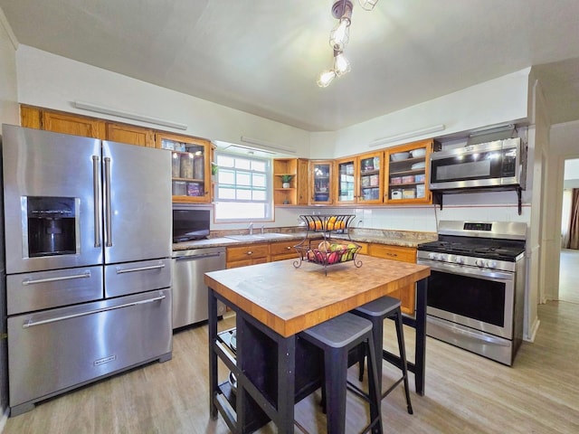 3715 Clinton Ave, Berwyn, IL 60402 - kitchen with stainless steel appliances, brown cabinetry, light wood finished floors, a sink, and glass insert cabinets