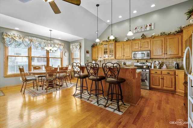 kitchen with brown cabinets, ceiling fan with notable chandelier, a kitchen breakfast bar, and stainless steel appliances