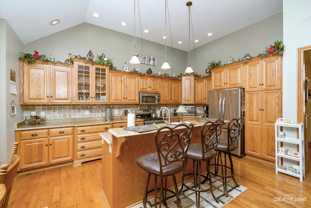kitchen with high vaulted ceiling, light wood-style flooring, a breakfast bar, and appliances with stainless steel finishes