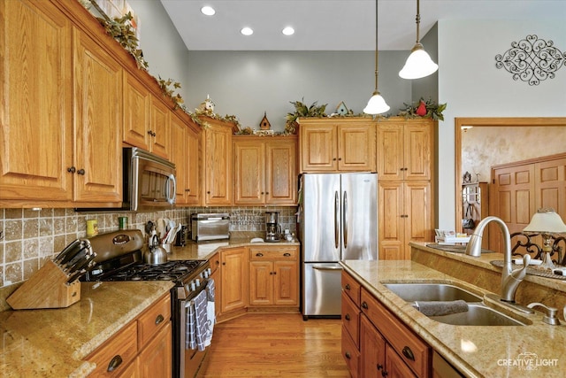 kitchen with decorative light fixtures, a sink, light stone countertops, backsplash, and stainless steel appliances