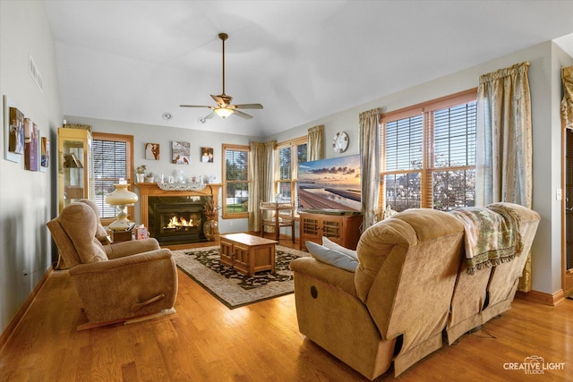 living area featuring ceiling fan, a lit fireplace, visible vents, wood finished floors, and lofted ceiling