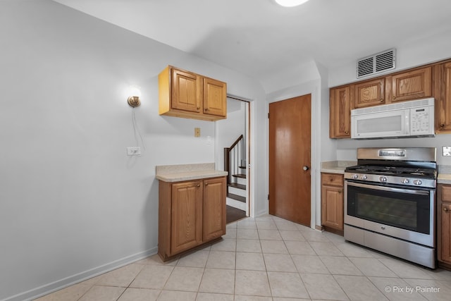 kitchen featuring white microwave, light tile patterned floors, visible vents, light countertops, and stainless steel gas range oven