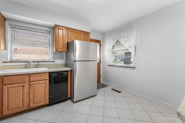 kitchen with black dishwasher, a sink, light countertops, freestanding refrigerator, and a wealth of natural light