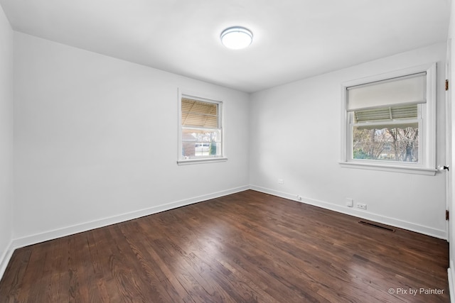 unfurnished room with visible vents, dark wood-style flooring, and baseboards