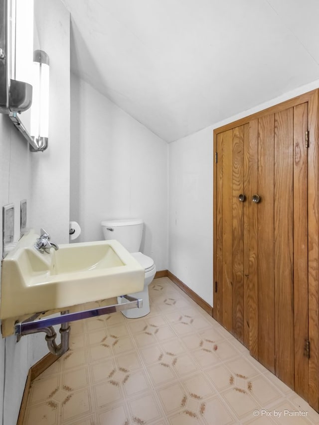 bathroom with baseboards, tile patterned floors, toilet, lofted ceiling, and a sink