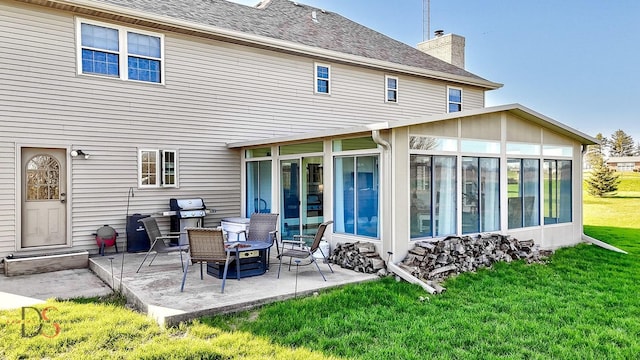rear view of house with a lawn, a patio area, a sunroom, and a chimney