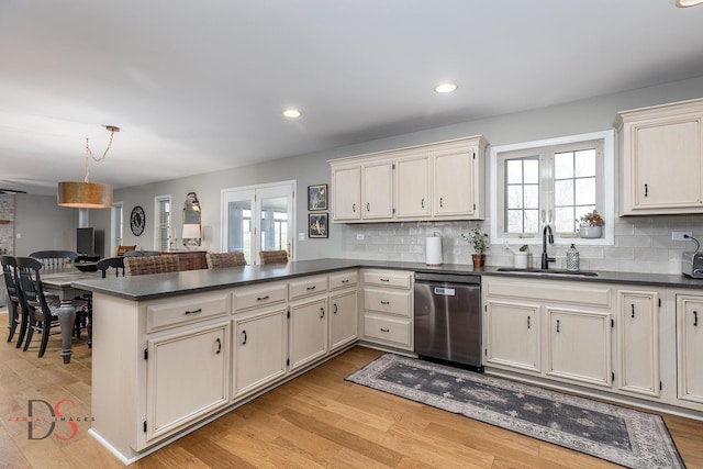 kitchen with a sink, dark countertops, light wood-style floors, a peninsula, and stainless steel dishwasher