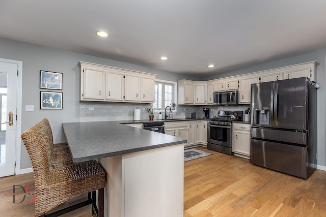 kitchen featuring stainless steel appliances, light wood finished floors, a peninsula, and dark countertops