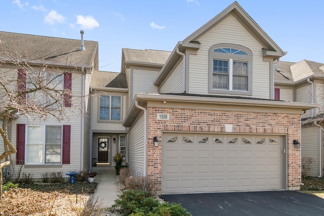 traditional home with brick siding, roof with shingles, an attached garage, and aphalt driveway