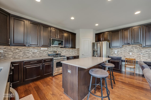 kitchen with decorative backsplash, appliances with stainless steel finishes, dark brown cabinets, and a kitchen bar