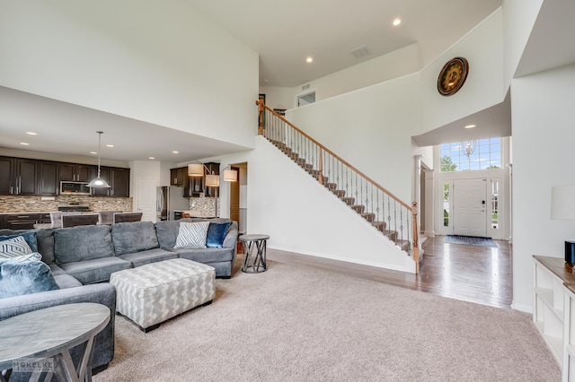 carpeted living room with visible vents, baseboards, a high ceiling, stairway, and recessed lighting