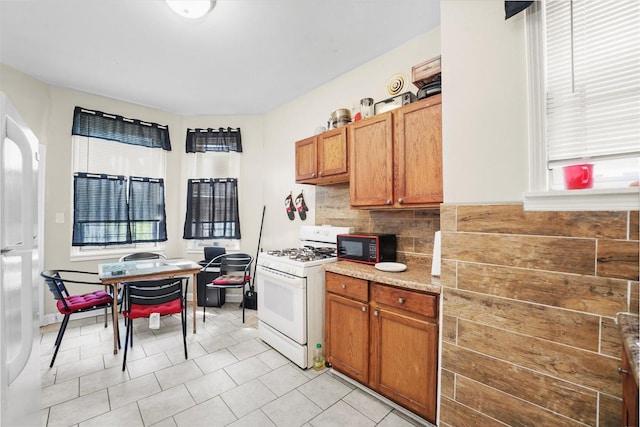 kitchen featuring a wealth of natural light, backsplash, black microwave, and white gas stove