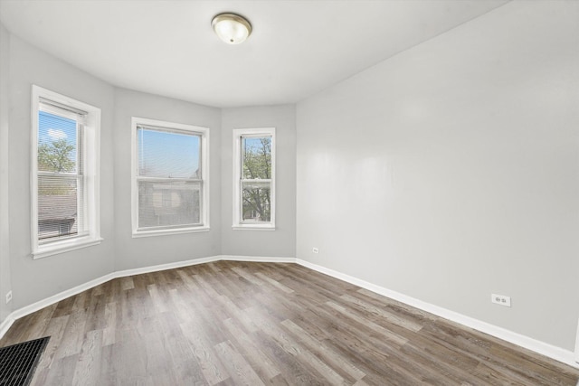 spare room featuring visible vents, baseboards, a healthy amount of sunlight, and wood finished floors