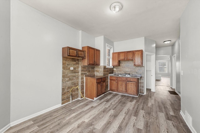 kitchen featuring brown cabinets, a sink, baseboards, light wood-style floors, and tasteful backsplash