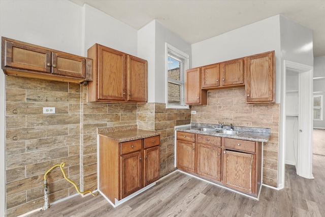 kitchen with brown cabinets, decorative backsplash, light wood-type flooring, and a sink