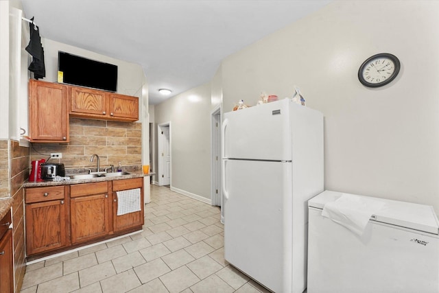 kitchen featuring freestanding refrigerator, light tile patterned floors, refrigerator, a sink, and backsplash