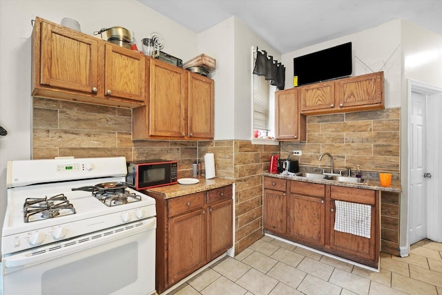 kitchen featuring a sink, brown cabinetry, gas range gas stove, black microwave, and light tile patterned floors