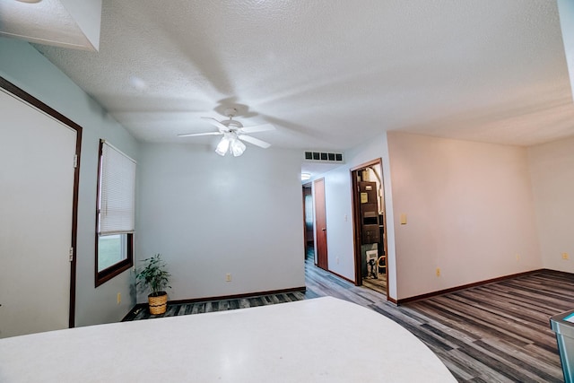 unfurnished bedroom featuring ceiling fan, a textured ceiling, visible vents, wood finished floors, and baseboards