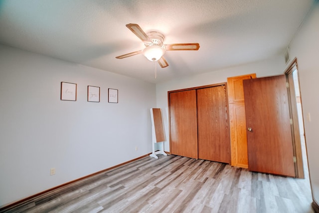 unfurnished bedroom featuring light wood-style flooring, a textured ceiling, a closet, a ceiling fan, and baseboards