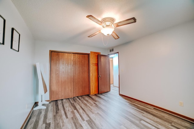 unfurnished bedroom with light wood-style floors, a textured ceiling, a closet, visible vents, and baseboards
