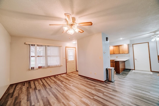 unfurnished living room with baseboards, light wood-style floors, a textured ceiling, and a ceiling fan