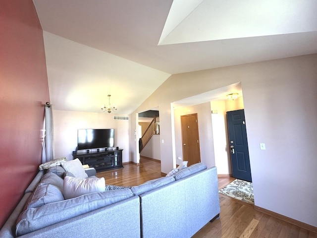 living room with wood finished floors, stairs, an inviting chandelier, lofted ceiling, and visible vents