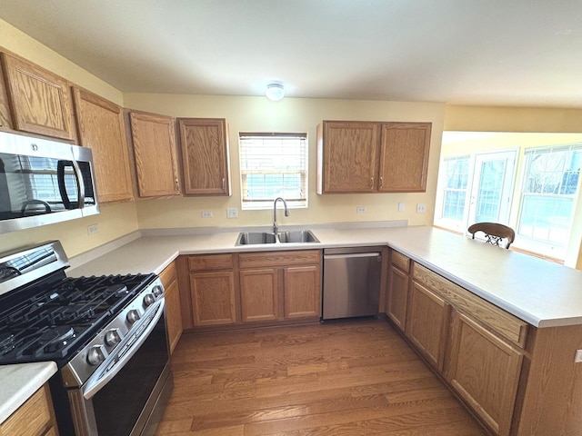 kitchen with stainless steel appliances, light countertops, wood finished floors, a sink, and a peninsula