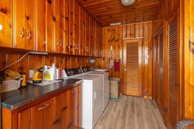 laundry room with light wood-style flooring, wood walls, washing machine and clothes dryer, and cabinet space