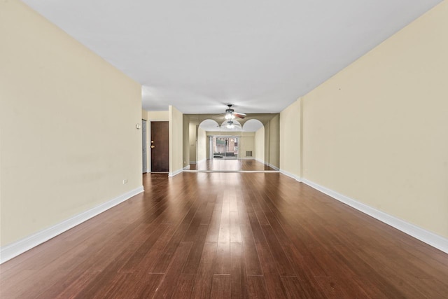 unfurnished living room with baseboards, a ceiling fan, arched walkways, and wood finished floors