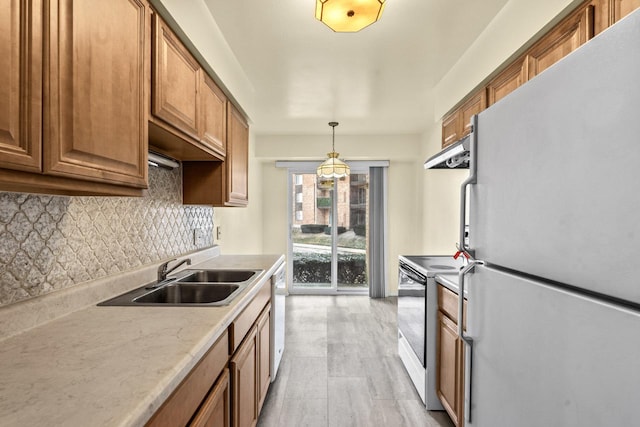kitchen with white appliances, under cabinet range hood, a sink, brown cabinets, and backsplash