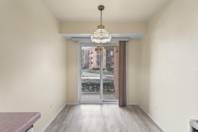 unfurnished dining area featuring baseboards, an inviting chandelier, and wood finished floors