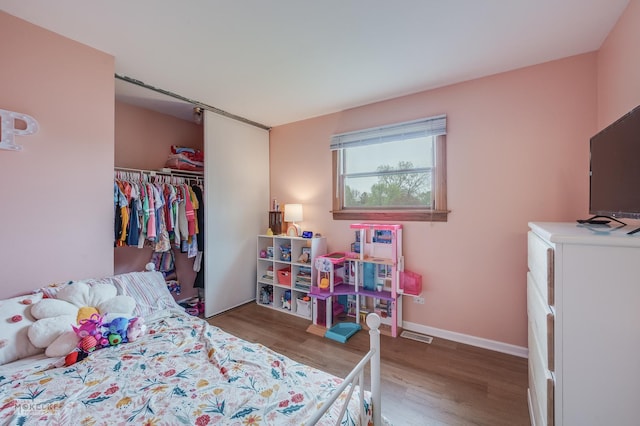 bedroom with baseboards, visible vents, wood finished floors, and a closet