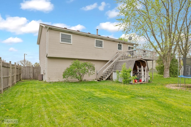 back of house with a trampoline, a wooden deck, fence, a yard, and stairs