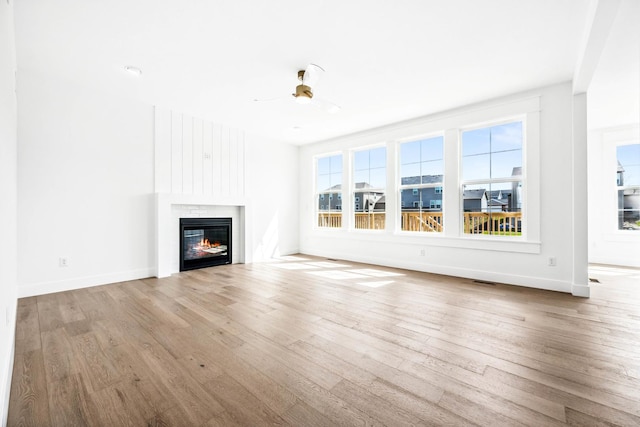 unfurnished living room featuring a ceiling fan, wood finished floors, baseboards, and a glass covered fireplace