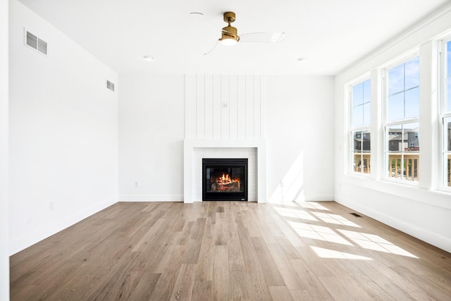 unfurnished living room with a large fireplace, visible vents, baseboards, and wood finished floors