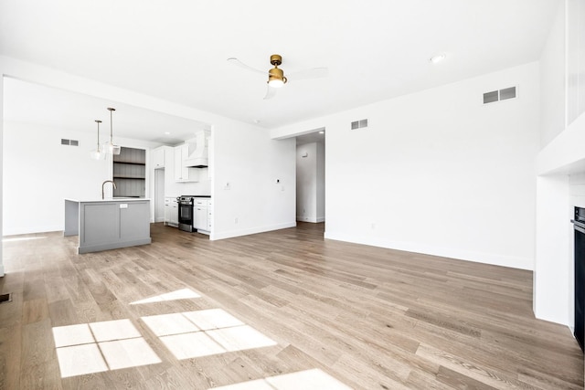unfurnished living room with light wood-style floors, ceiling fan, a sink, and visible vents