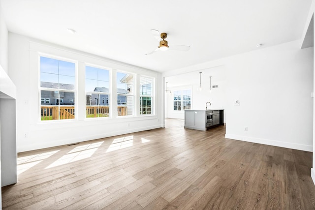unfurnished living room with a sink, ceiling fan, wood finished floors, and baseboards