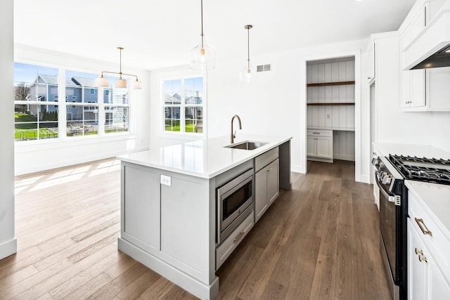 kitchen with custom exhaust hood, visible vents, a sink, stainless steel microwave, and gas stove