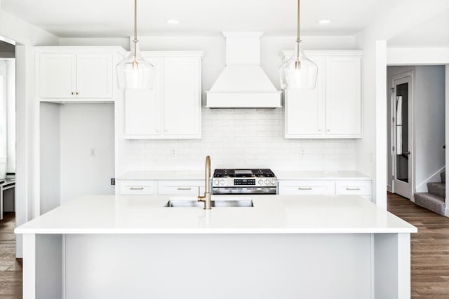 kitchen featuring custom exhaust hood, gas range, a sink, light countertops, and an island with sink